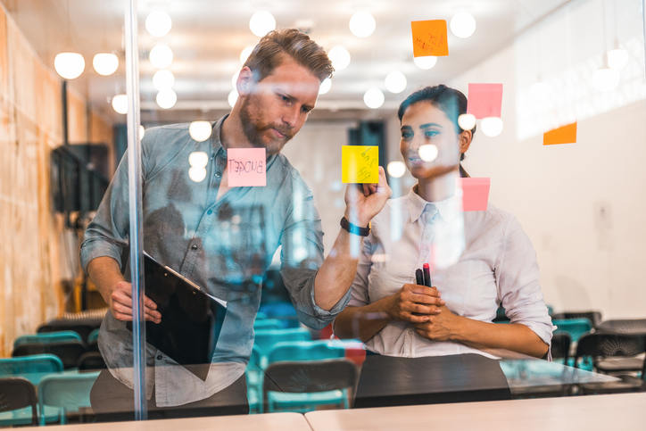 Zwei Personen besprechen sich an einer durchsichtigen Wand mit Post Its