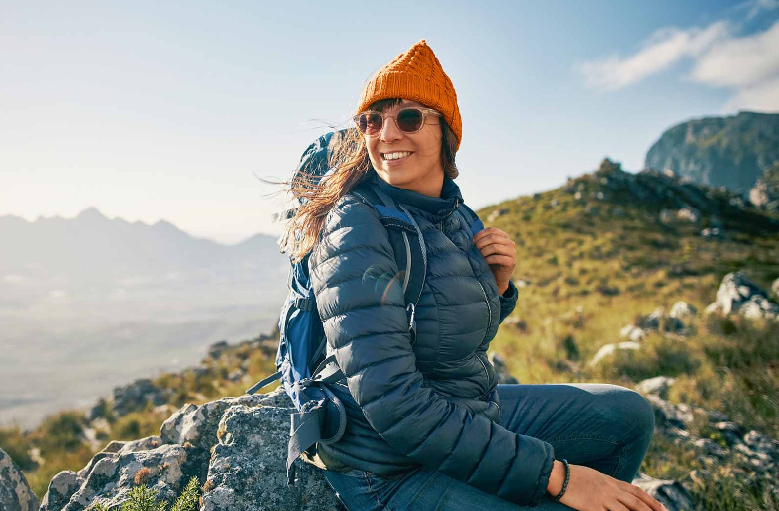 Eine junge Frau sitzt auf einem Berggipfel und lacht.