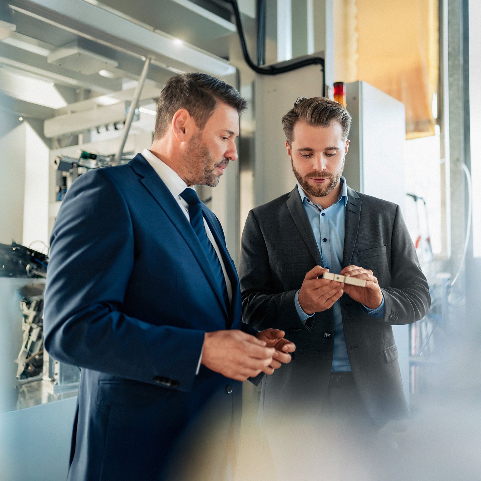 Zwei Männer stehen vor einer Maschine und halten ein technisches Gerät in der Hand.