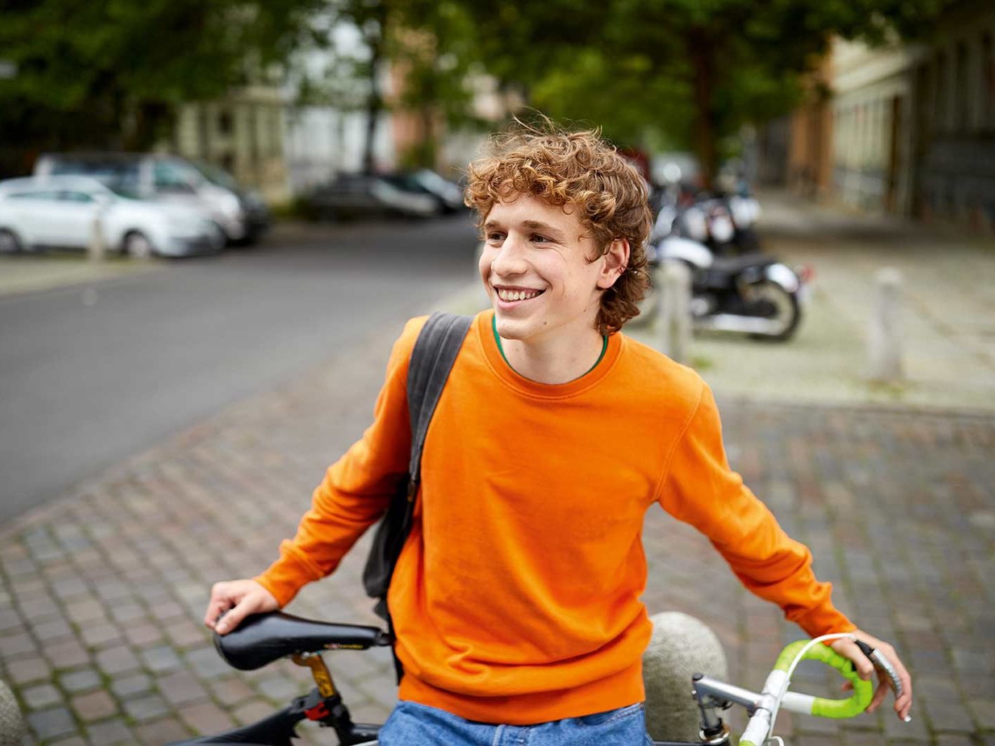 Ein jugendlicher Mann steht mit seinem Fahrrad auf einer Straße und lächelt