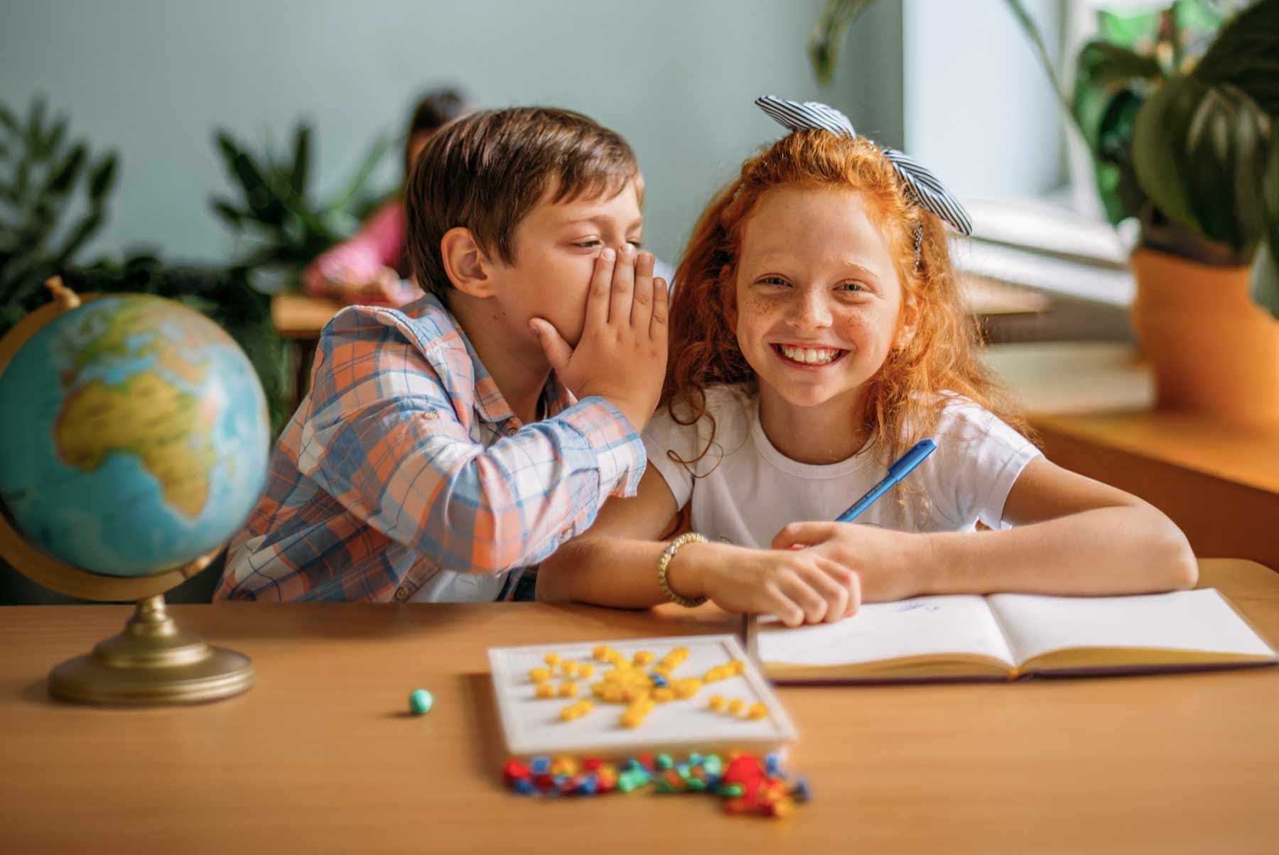 Ein Junge und ein Mädchen sitzen im Klassenzimmer und lachen.